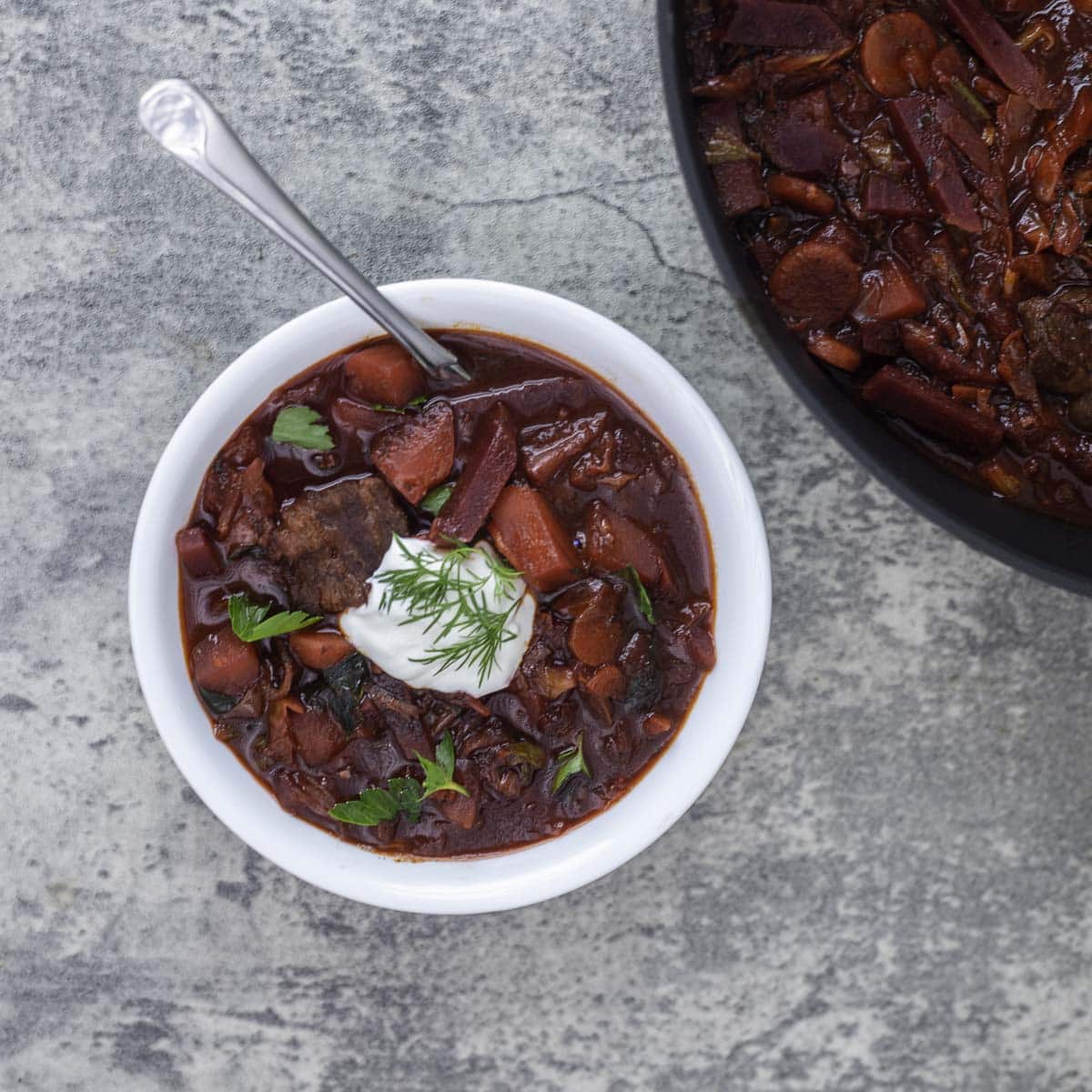 Ukrainian borscht recipe in a white bowl with more in a pot